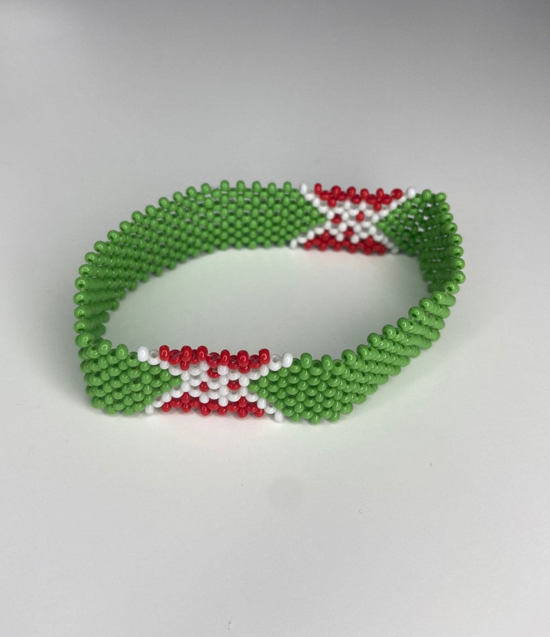 May include: A green beaded bracelet with red and white beads forming a cross pattern. The bracelet is made of small, round beads.