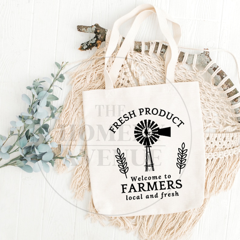 Pu&ograve; includere: Una borsa di tela bianca con testo nero e un grafico di un mulino a vento. Il testo dice "The Fresh Product" con uno stelo di grano su entrambi i lati del mulino a vento. Sotto il mulino a vento, il testo dice "Welcome to Farmers local and fresh".