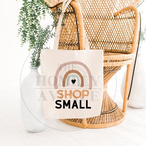 Pu&ograve; includere: Una borsa di tela bianca con un design a arcobaleno e il testo "Shop Small" in nero. L'arcobaleno ha un piccolo cuore nero al centro.