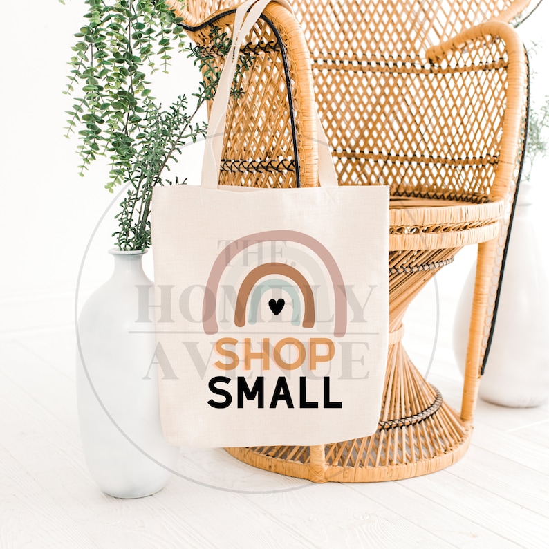 Pu&ograve; includere: Una borsa di tela bianca con un design a arcobaleno e il testo "Shop Small" in nero. L'arcobaleno ha un piccolo cuore nero al centro.