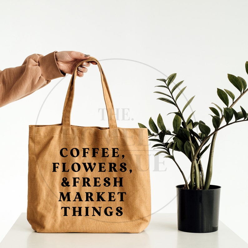 Pu&ograve; includere: Una borsa di tela marrone con testo nero che recita "COFFEE, FLOWERS, & FRESH MARKET THINGS".
