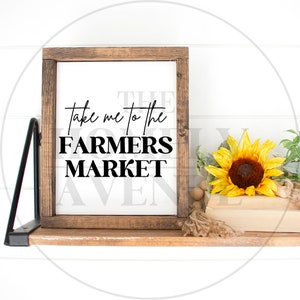 May include: A wooden sign with the text "Take me to the Farmers Market" in black lettering on a white background. The sign is sitting on a wooden shelf with a sunflower and a string of wooden beads.