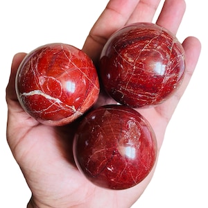 May include: Three red jasper spheres with white veins. The spheres are smooth and polished.