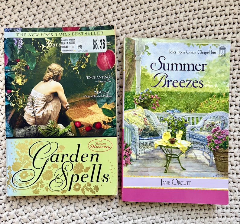 May include: Two paperback books. "Garden Spells" by Sara and "Summer Breezes" by Jane Orcutt. "Garden Spells" has a woman on the cover, with a green and gold title. "Summer Breezes" has a porch scene with wicker furniture.
