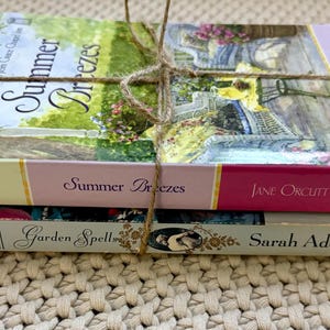 May include: A stack of three books tied with twine. The top book is titled "Summer Breezes" with a floral cover. The middle book is titled "Summer Breezes" by Jane Orcutt. The bottom book is titled "Garden Spell" by Sarah Addison Allen.