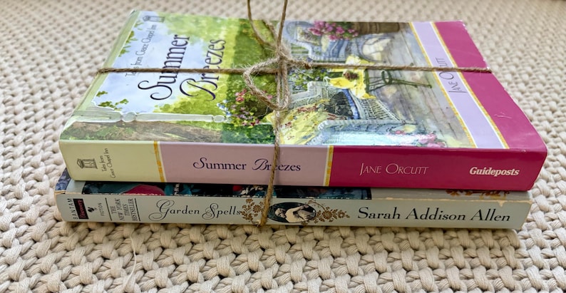 May include: A stack of three books tied with twine. The top book is titled "Summer Breezes" with a floral cover. The middle book is titled "Summer Breezes" by Jane Orcutt. The bottom book is titled "Garden Spell" by Sarah Addison Allen.