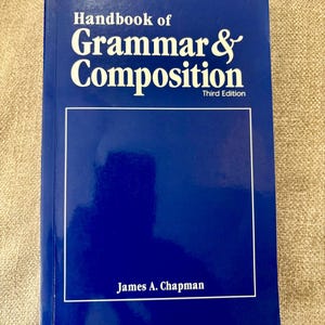 May include: A blue textbook titled "Handbook of Grammar & Composition, Third Edition" with white lettering. The author's name, James A. Chapman, is printed at the bottom. The book has a white border around a blank space.