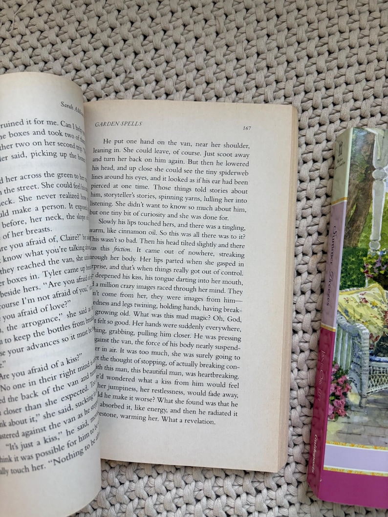 May include: Open book with text from "Garden Spells" by Sarah Addison Allen. The page is open to chapter 167. A bookmark with a floral design is visible on the right side of the book.