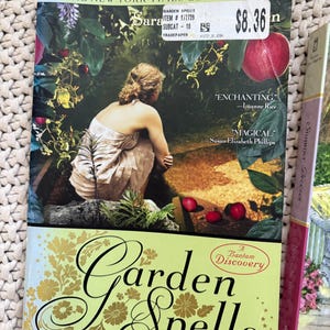May include: A paperback book titled "Garden Spells" by Sarah Addison Allen. The cover features a woman in a garden setting with red apples. The book is a New York Times bestseller and includes quotes from Luanne Rice and Susan Elizabeth Phillips.