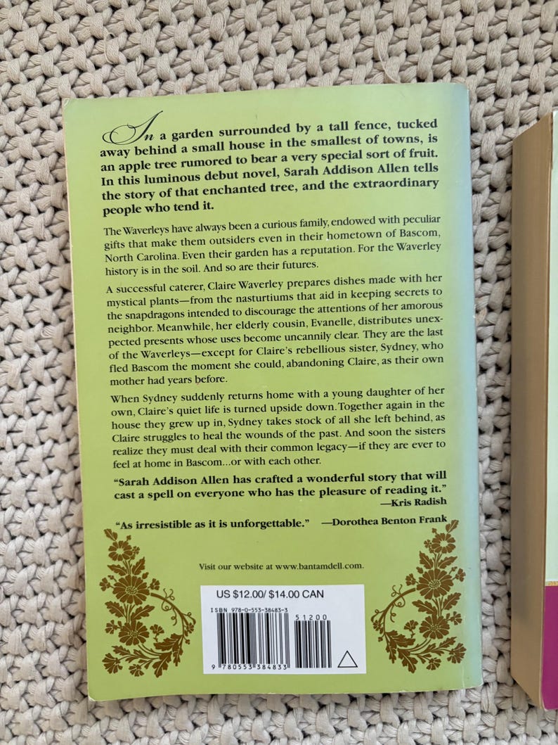 May include: A book cover with a green background and floral design. The title and author's name are not visible. The back cover text describes a novel about a family with peculiar gifts and an enchanted tree. The price is $12.00.