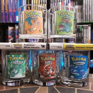 May include: Six clear glass tumblers with colorful Pokemon game cartridge designs. The designs include:  "Pokemon FireRed Version", "Pokemon LeafGreen Version", "Pokemon Emerald Version", "Pokemon Ruby Version", "Pokemon Sapphire Version", and "Pokemon White Version".
