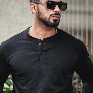 Puede incluir: Una camisa negra de manga larga con cuello abotonado. La camisa tiene un corte holgado y está hecha de una tela suave y cómoda.