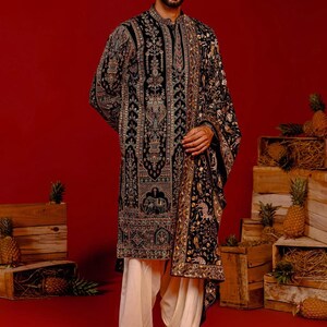 Man wearing an opulent black Mughal-style kurta with intricate multicolor embroidery, paired with cream Patiala trousers and a heavily embellished dupatta featuring animal and floral motifs—ideal for grooms, traditional South Asian weddings, and cultural festivities.