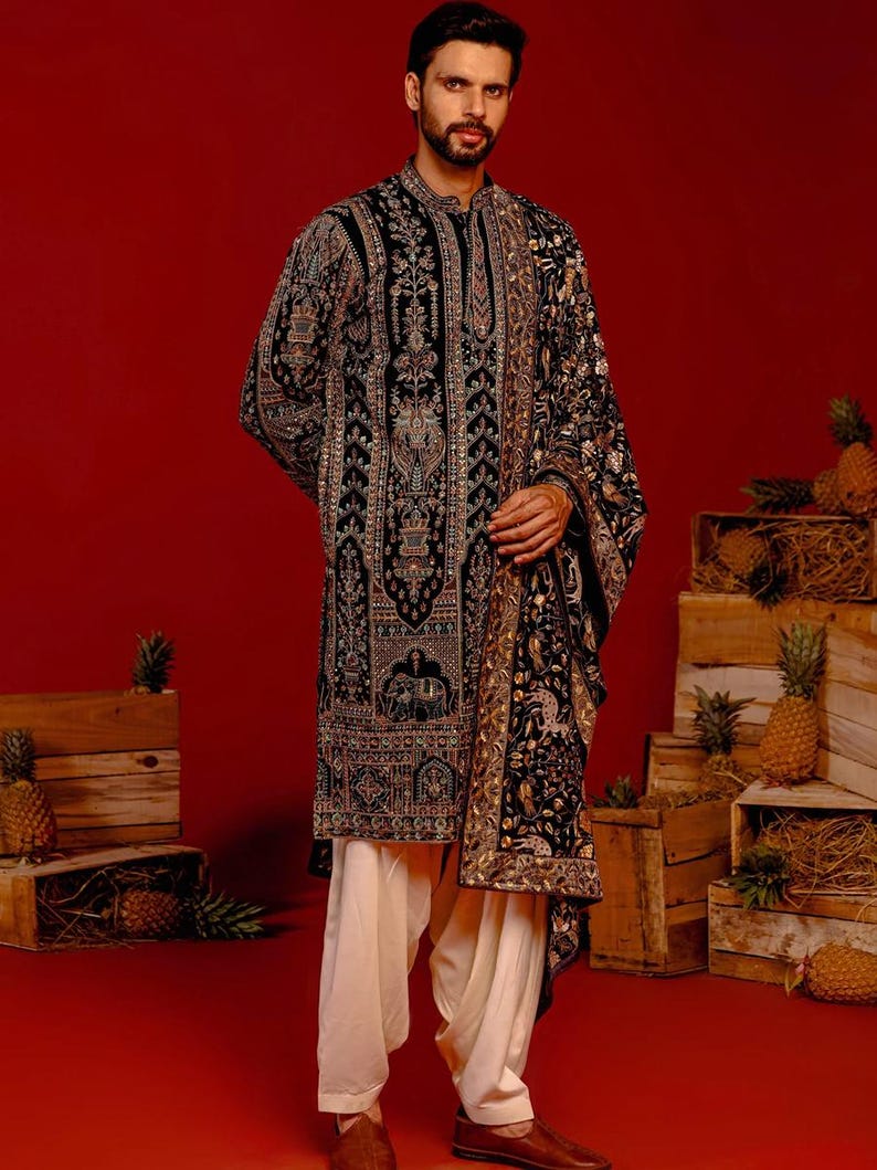 Man wearing an opulent black Mughal-style kurta with intricate multicolor embroidery, paired with cream Patiala trousers and a heavily embellished dupatta featuring animal and floral motifs—ideal for grooms, traditional South Asian weddings, and cultural festivities.