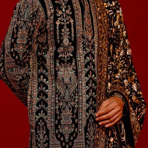 Man wearing an opulent black Mughal-style kurta with intricate multicolor embroidery, paired with cream Patiala trousers and a heavily embellished dupatta featuring animal and floral motifs—ideal for grooms, traditional South Asian weddings, and cultural festivities.