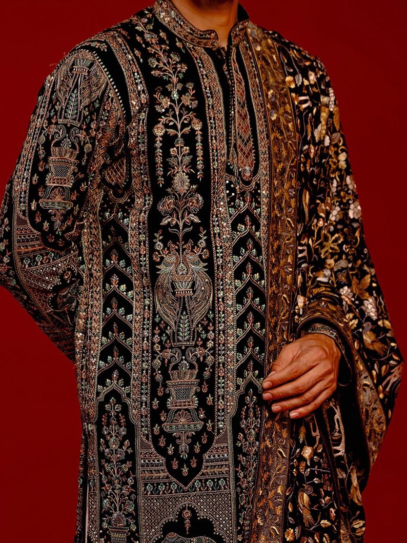 Man wearing an opulent black Mughal-style kurta with intricate multicolor embroidery, paired with cream Patiala trousers and a heavily embellished dupatta featuring animal and floral motifs—ideal for grooms, traditional South Asian weddings, and cultural festivities.