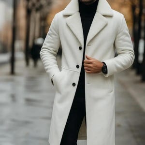 May include: A long, off-white coat with a black turtleneck and black pants. The coat has a wide collar with a fuzzy lining and three black buttons. A black watch is visible on the wrist.