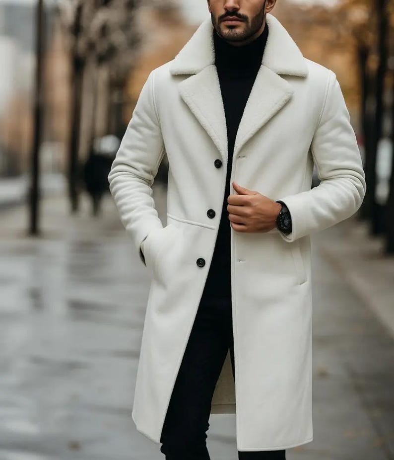 May include: A long, off-white coat with a black turtleneck and black pants. The coat has a wide collar with a fuzzy lining and three black buttons. A black watch is visible on the wrist.