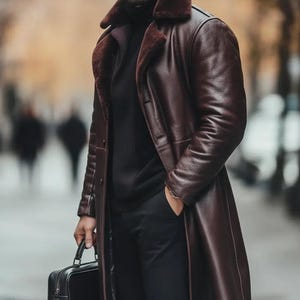 May include: A long, dark brown leather coat with a shearling collar. The coat is worn over a black turtleneck and black pants. A black briefcase is held in one hand.