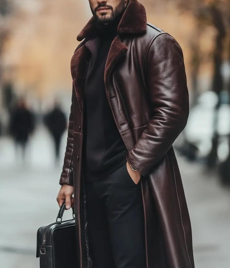 May include: A long, dark brown leather coat with a shearling collar. The coat is worn over a black turtleneck and black pants. A black briefcase is held in one hand.