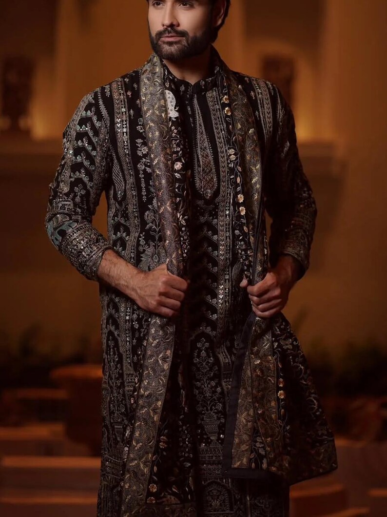 Man wearing an opulent black Mughal-style kurta with intricate multicolor embroidery, paired with cream Patiala trousers and a heavily embellished dupatta featuring animal and floral motifs—ideal for grooms, traditional South Asian weddings, and cultural festivities.