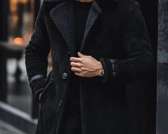 May include: A black, knee-length coat with a shearling collar and lining. The coat features a button-down closure, side pockets, and buttoned cuffs. The coat is made of a suede-like material.