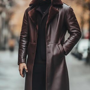 May include: A long, dark brown leather coat with a faux fur collar. The coat has a button-down front, pockets, and a tailored fit. The coat is worn over a black turtleneck and black pants. The person is holding a black phone.
