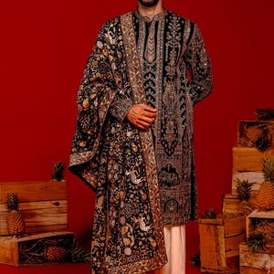 Man wearing an opulent black Mughal-style kurta with intricate multicolor embroidery, paired with cream Patiala trousers and a heavily embellished dupatta featuring animal and floral motifs—ideal for grooms, traditional South Asian weddings, and cultural festivities.