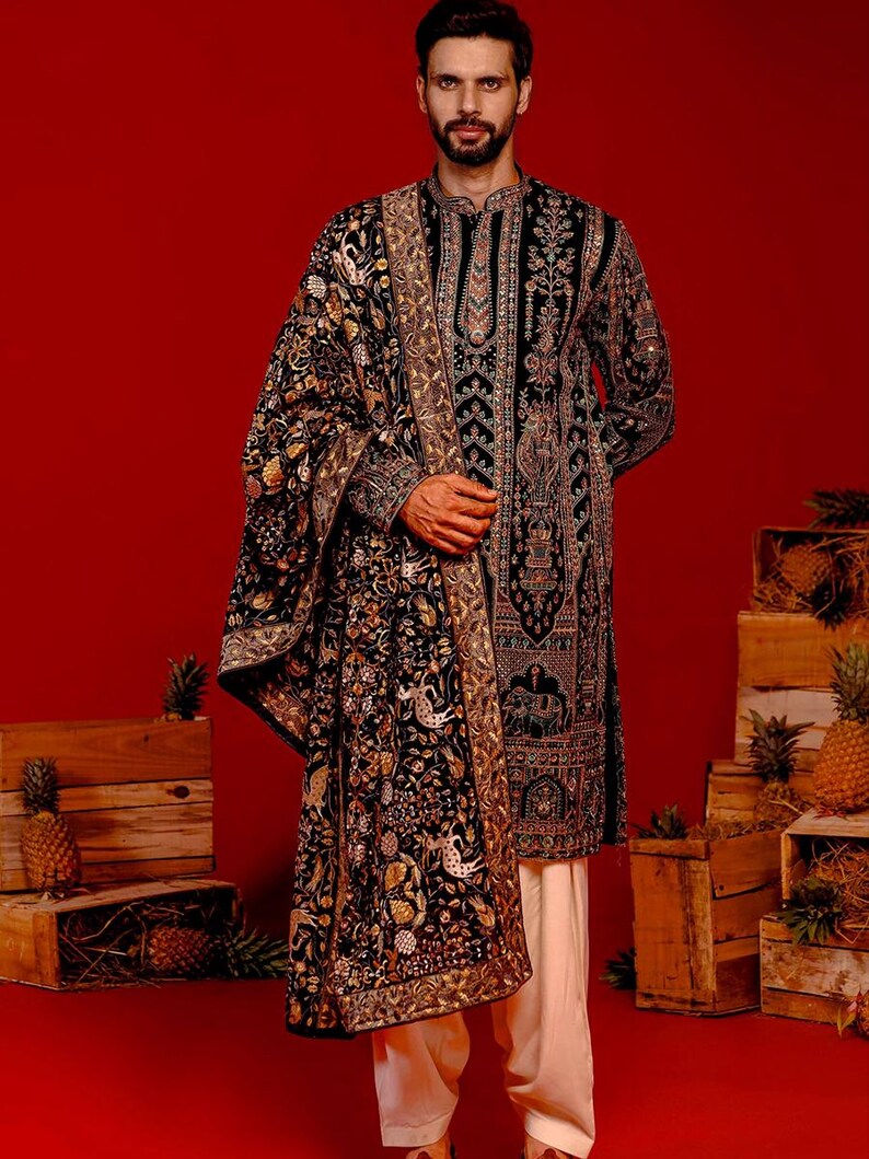 Man wearing an opulent black Mughal-style kurta with intricate multicolor embroidery, paired with cream Patiala trousers and a heavily embellished dupatta featuring animal and floral motifs—ideal for grooms, traditional South Asian weddings, and cultural festivities.