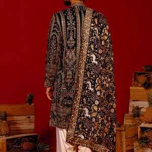 Man wearing an opulent black Mughal-style kurta with intricate multicolor embroidery, paired with cream Patiala trousers and a heavily embellished dupatta featuring animal and floral motifs—ideal for grooms, traditional South Asian weddings, and cultural festivities.
