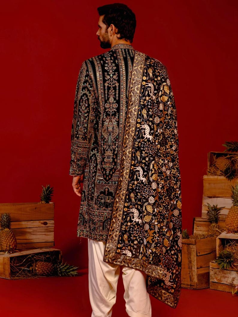Man wearing an opulent black Mughal-style kurta with intricate multicolor embroidery, paired with cream Patiala trousers and a heavily embellished dupatta featuring animal and floral motifs—ideal for grooms, traditional South Asian weddings, and cultural festivities.
