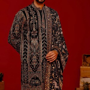 Man wearing an opulent black Mughal-style kurta with intricate multicolor embroidery, paired with cream Patiala trousers and a heavily embellished dupatta featuring animal and floral motifs—ideal for grooms, traditional South Asian weddings, and cultural festivities.