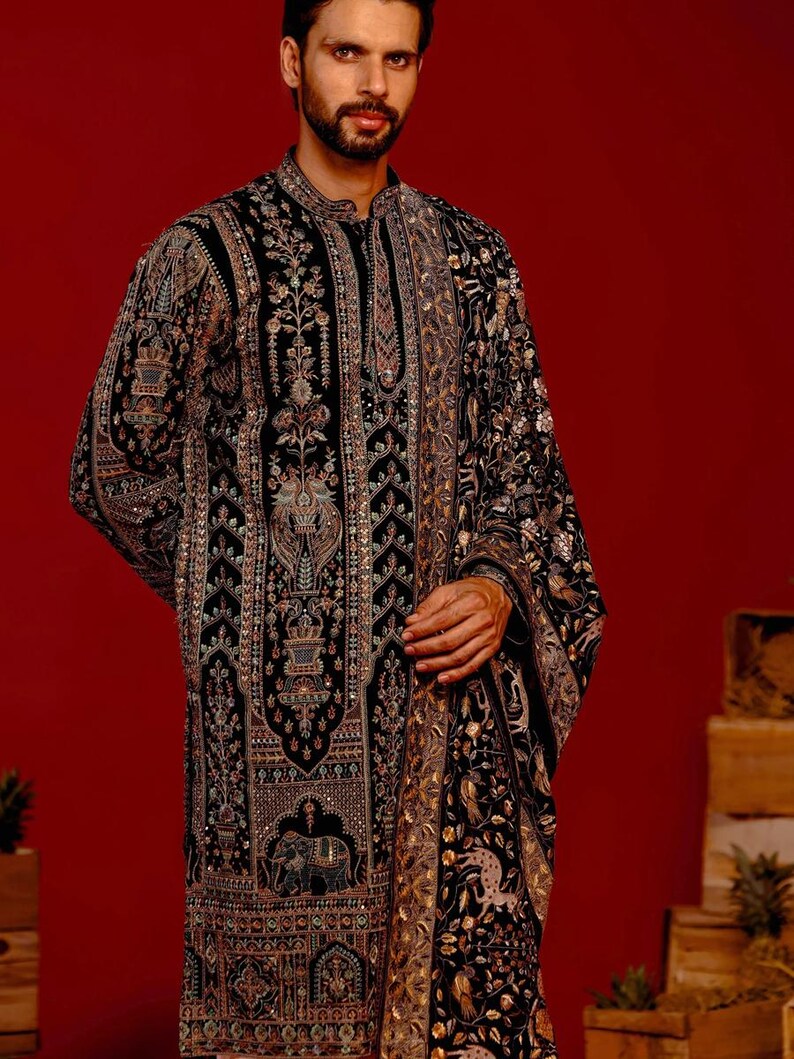 Man wearing an opulent black Mughal-style kurta with intricate multicolor embroidery, paired with cream Patiala trousers and a heavily embellished dupatta featuring animal and floral motifs—ideal for grooms, traditional South Asian weddings, and cultural festivities.
