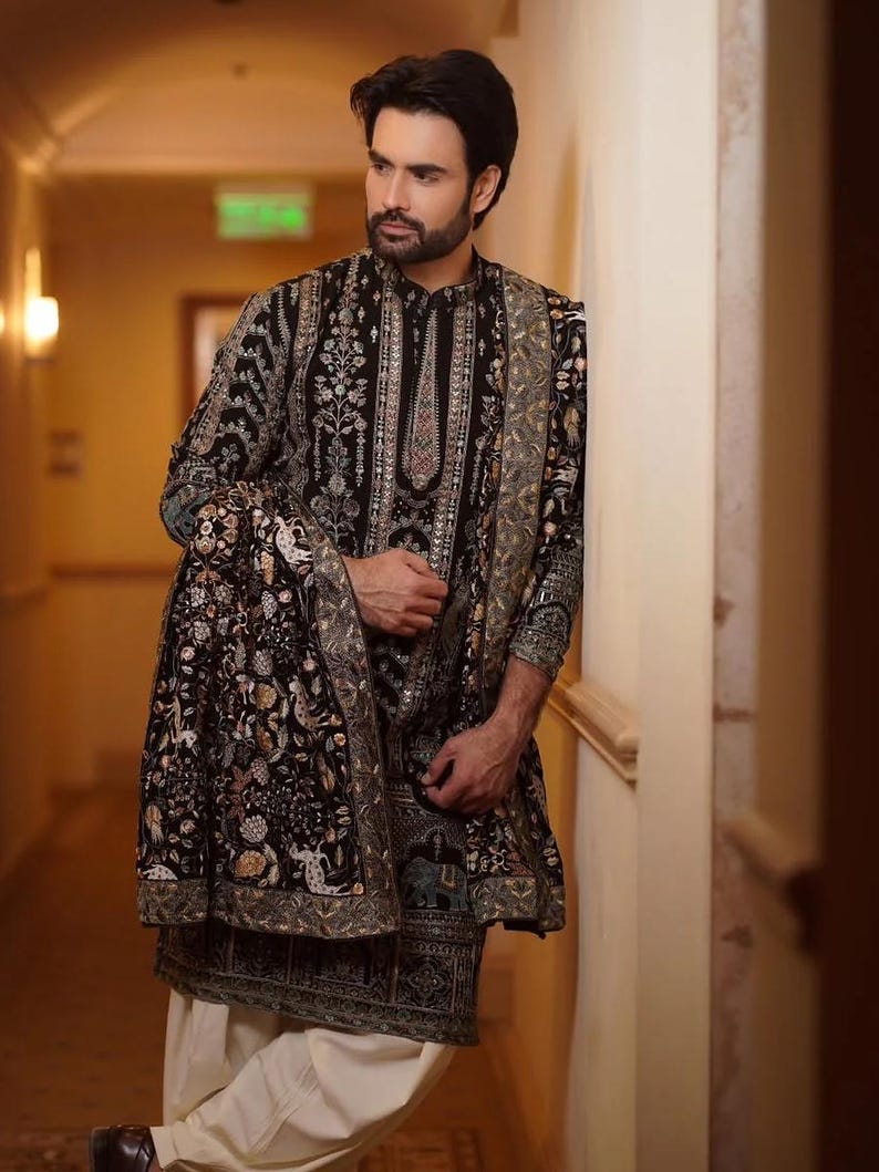 Man wearing an opulent black Mughal-style kurta with intricate multicolor embroidery, paired with cream Patiala trousers and a heavily embellished dupatta featuring animal and floral motifs—ideal for grooms, traditional South Asian weddings, and cultural festivities.