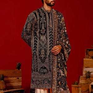 Man wearing an opulent black Mughal-style kurta with intricate multicolor embroidery, paired with cream Patiala trousers and a heavily embellished dupatta featuring animal and floral motifs—ideal for grooms, traditional South Asian weddings, and cultural festivities.