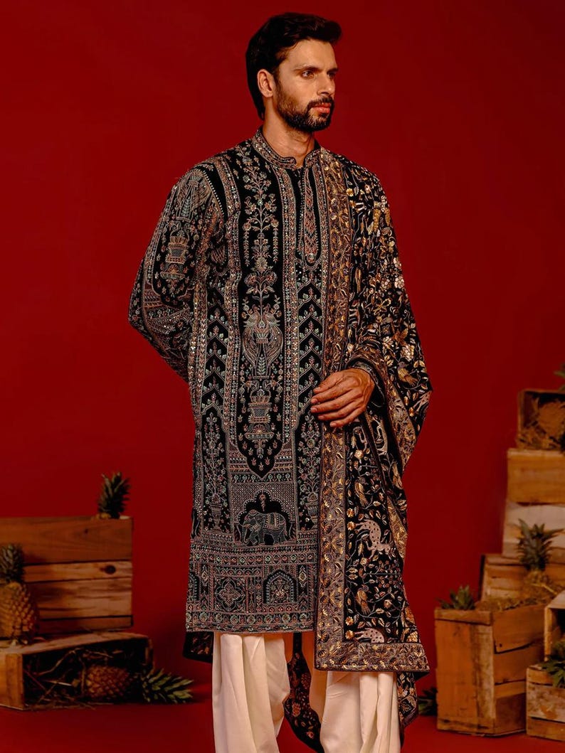 Man wearing an opulent black Mughal-style kurta with intricate multicolor embroidery, paired with cream Patiala trousers and a heavily embellished dupatta featuring animal and floral motifs—ideal for grooms, traditional South Asian weddings, and cultural festivities.