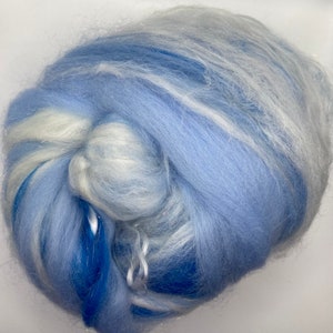 Puede incluir: Primer plano de una nube de fibra en tonos azules y blancos. La fibra es suave y esponjosa, con hebras de purpurina plateada. Los colores se mezclan, creando un efecto so&ntilde;ador y et&eacute;reo. Esta fibra se utiliza probablemente para manualidades.