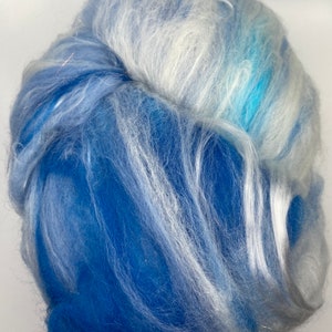 Puede incluir: Primer plano de un manojo de fibra azul y blanca. La fibra es una mezcla de azules claros y oscuros con vetas blancas, creando una apariencia suave y texturizada. Las fibras est&aacute;n muy juntas, formando una forma densa, similar a una nube.