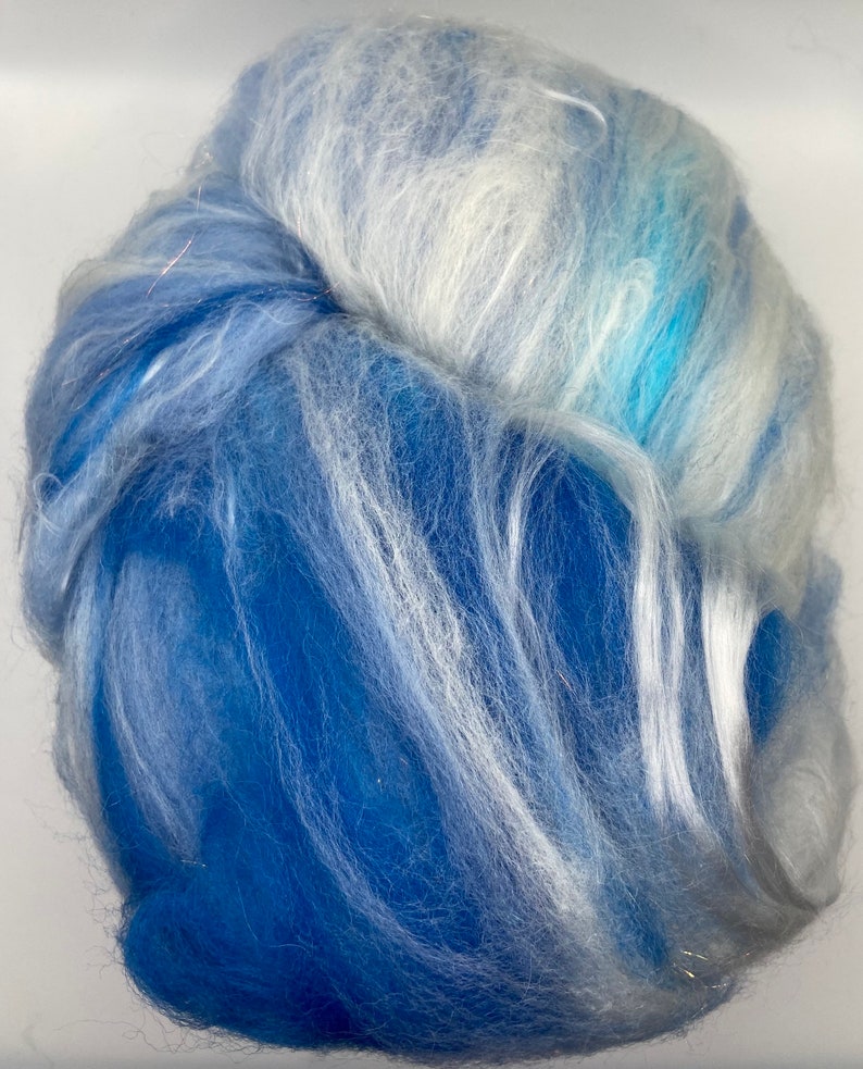 Puede incluir: Primer plano de un manojo de fibra azul y blanca. La fibra es una mezcla de azules claros y oscuros con vetas blancas, creando una apariencia suave y texturizada. Las fibras est&aacute;n muy juntas, formando una forma densa, similar a una nube.