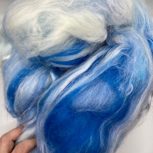 Puede incluir: Primer plano de una nube de fibra en tonos azules y blancos. La fibra es suave y esponjosa, con una mezcla de tonos azules claros y oscuros. La textura parece delicada y aireada, adecuada para proyectos de manualidades.