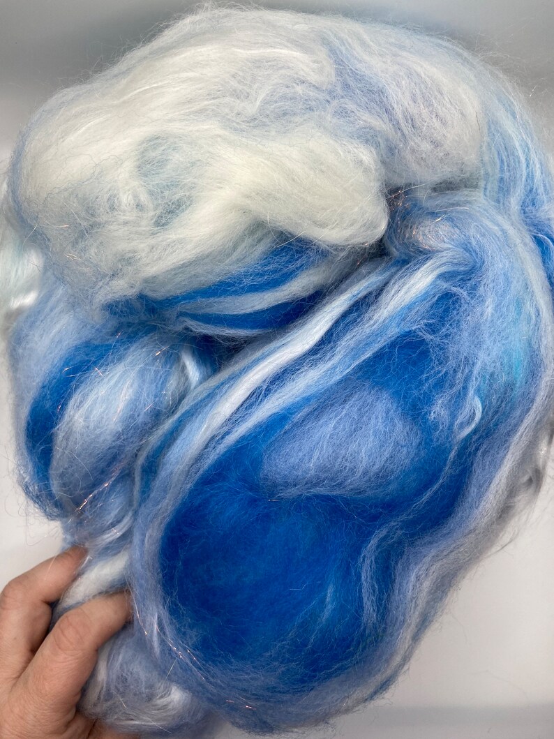 Puede incluir: Primer plano de una nube de fibra en tonos azules y blancos. La fibra es suave y esponjosa, con una mezcla de tonos azules claros y oscuros. La textura parece delicada y aireada, adecuada para proyectos de manualidades.