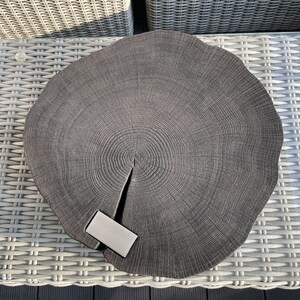 May include: A dark gray wooden serving tray with a natural wood grain pattern. The tray is round and has a slightly raised edge. A small, rectangular, silver-colored object is placed on the tray.