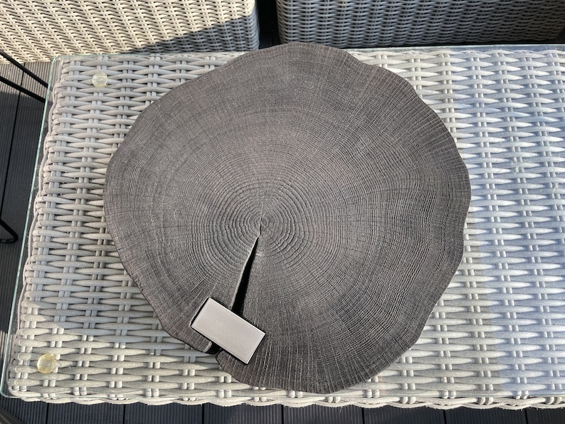 May include: A dark gray wooden serving tray with a natural wood grain pattern. The tray is round and has a slightly raised edge. A small, rectangular, silver-colored object is placed on the tray.