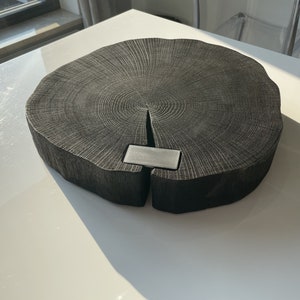 May include: A large, round, black wooden cutting board with a natural wood grain pattern. The board has a metal insert in the center.