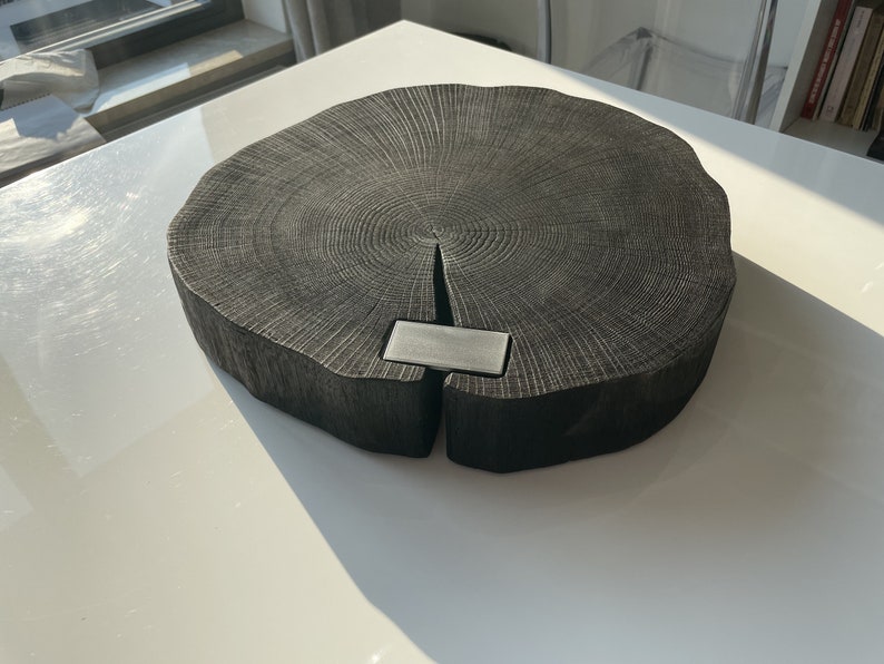May include: A large, round, black wooden cutting board with a natural wood grain pattern. The board has a metal insert in the center.