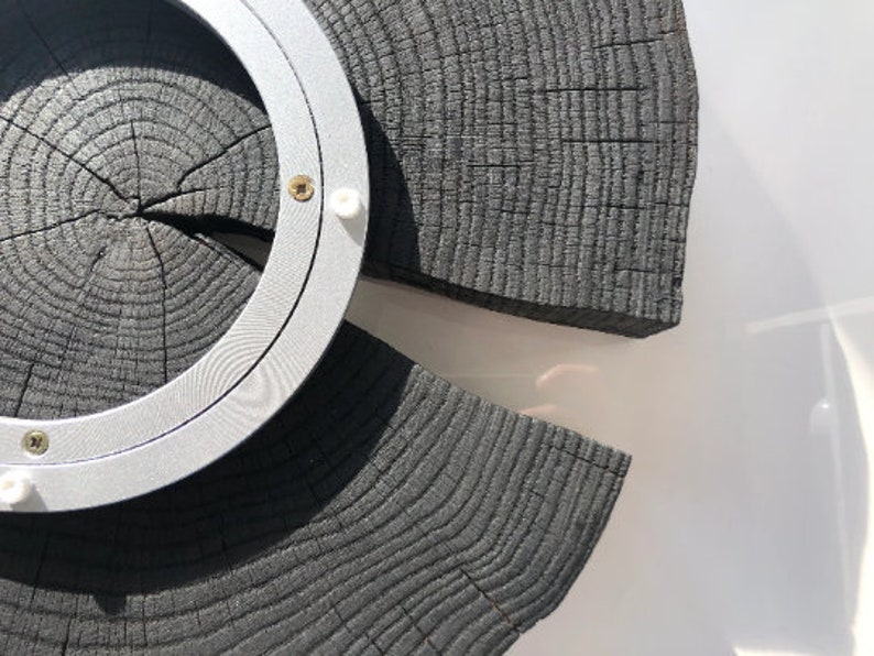 May include: A circular wooden wall decor with a silver metal ring around the center. The wood is dark gray and has a natural wood grain pattern.