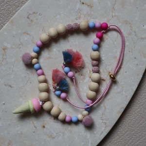 Könnte beinhalten: Eine rosa und blaue Perlenkette mit Holzperlen, rosa und blauen Quasten und einem rosa und gelben Eiscreme-Anhänger.