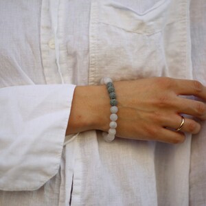 Könnte beinhalten: Ein weißes und graues Armband mit einem Lavastein-Design. Das Armband wird am Handgelenk getragen.
