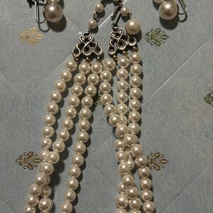 May include: A three-strand pearl necklace with a silver clasp and matching clip-on earrings. The pearls are white and round.