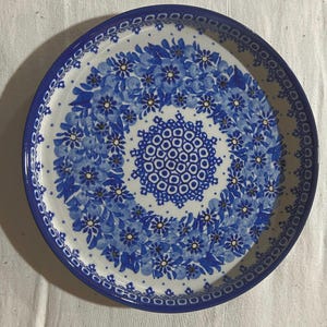 May include: A white ceramic plate with a blue and white floral design. The plate has a raised rim and a scalloped edge.